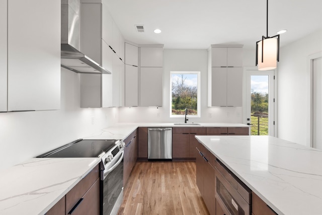 kitchen with light stone countertops, pendant lighting, appliances with stainless steel finishes, and wall chimney range hood