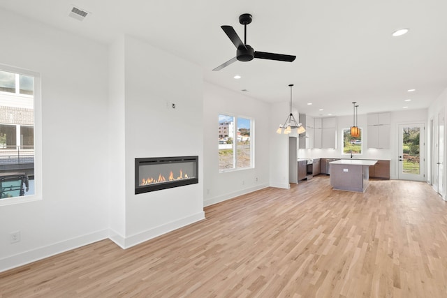 unfurnished living room featuring ceiling fan with notable chandelier and light hardwood / wood-style flooring