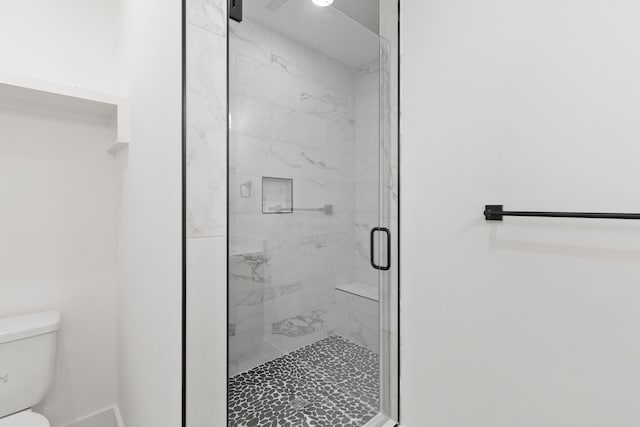 bathroom featuring a shower with shower door and toilet