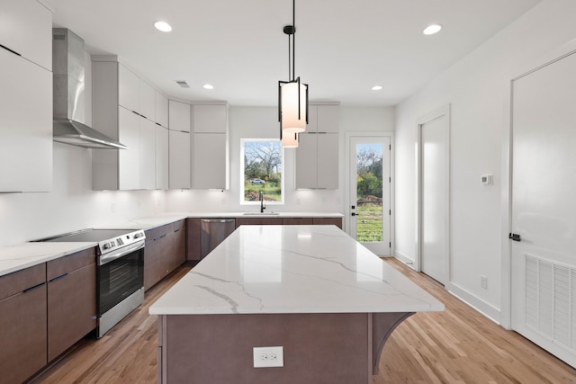 kitchen featuring a center island, wall chimney exhaust hood, decorative light fixtures, appliances with stainless steel finishes, and light wood-type flooring