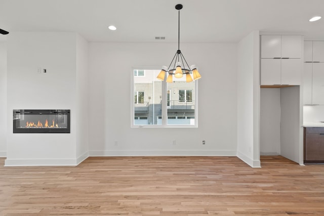 unfurnished dining area with light hardwood / wood-style floors and an inviting chandelier