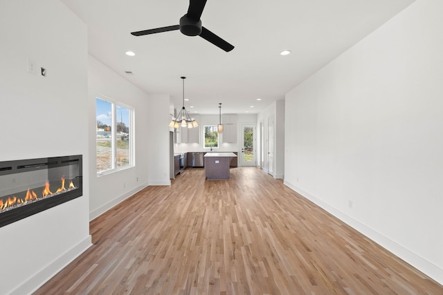 unfurnished living room featuring ceiling fan with notable chandelier and light hardwood / wood-style flooring