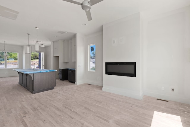 kitchen with a center island with sink, light wood-type flooring, decorative light fixtures, sink, and ceiling fan