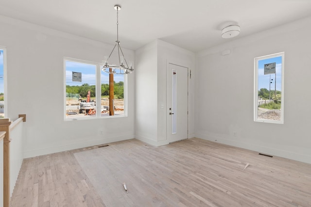 unfurnished dining area with light hardwood / wood-style floors, a notable chandelier, and a healthy amount of sunlight