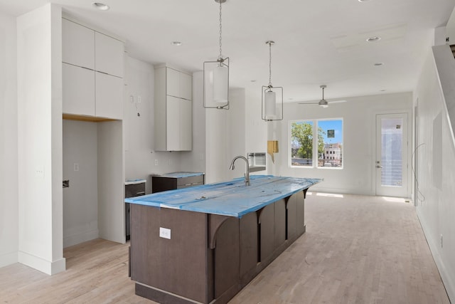 kitchen with hanging light fixtures, an island with sink, ceiling fan, white cabinetry, and light hardwood / wood-style flooring