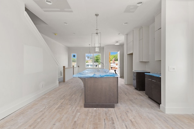 kitchen with light wood-type flooring, hanging light fixtures, a center island with sink, and white cabinetry