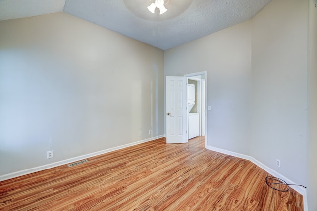 spare room featuring light hardwood / wood-style floors, lofted ceiling, and a textured ceiling