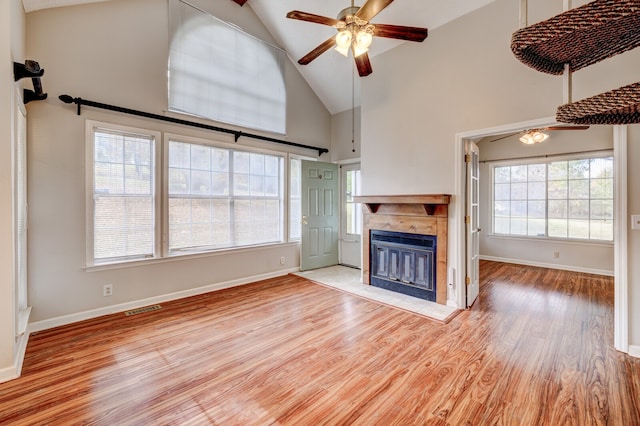 unfurnished living room featuring ceiling fan, a tile fireplace, light hardwood / wood-style flooring, and high vaulted ceiling