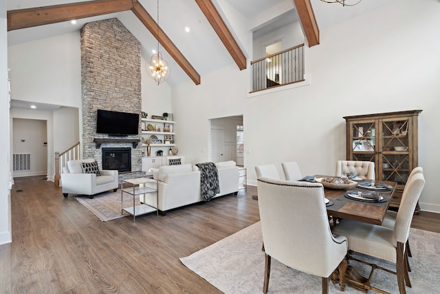 dining space with beamed ceiling, hardwood / wood-style flooring, a stone fireplace, and high vaulted ceiling