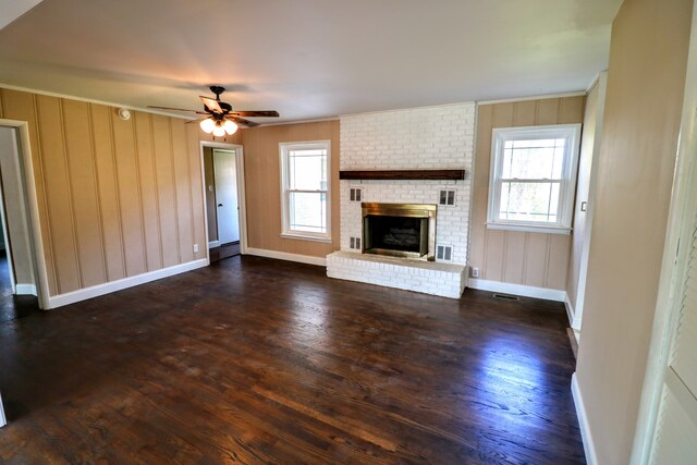 unfurnished living room featuring ceiling fan, a brick fireplace, a healthy amount of sunlight, and dark hardwood / wood-style floors