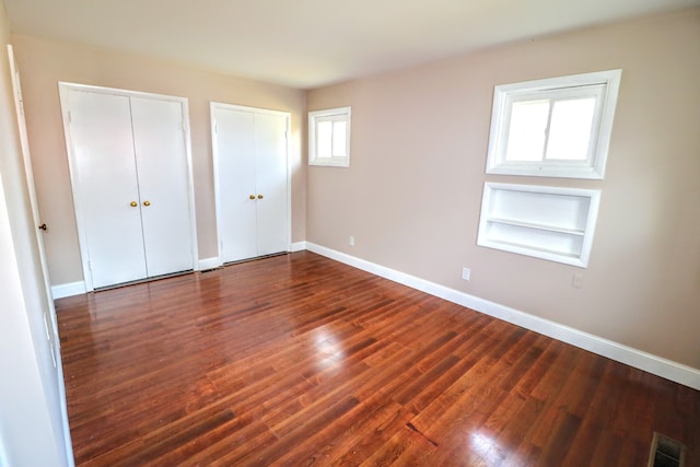 unfurnished bedroom with multiple closets and dark hardwood / wood-style floors