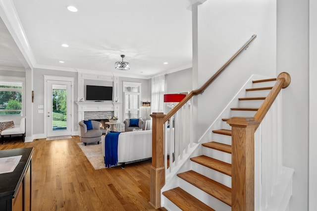 living room with light hardwood / wood-style floors, a stone fireplace, and crown molding