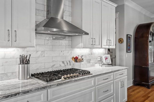 kitchen featuring wall chimney exhaust hood, backsplash, wood-type flooring, stainless steel gas stovetop, and white cabinets