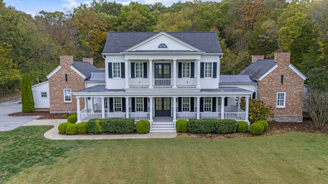 greek revival inspired property featuring covered porch, a front yard, and a balcony