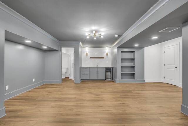 unfurnished living room with built in shelves, light wood-type flooring, a chandelier, and crown molding