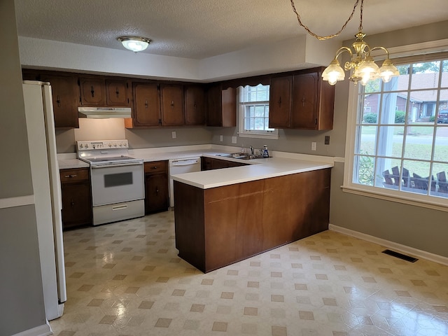 kitchen with sink, kitchen peninsula, white appliances, a chandelier, and pendant lighting