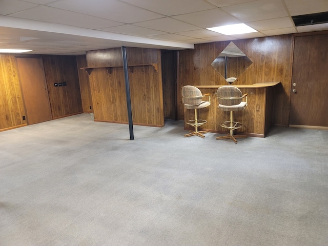 bar with a paneled ceiling, wooden walls, and light colored carpet