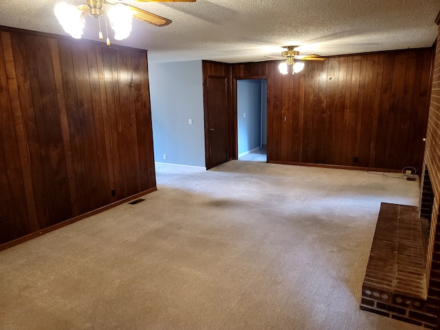 empty room featuring wooden walls, a textured ceiling, light colored carpet, and ceiling fan