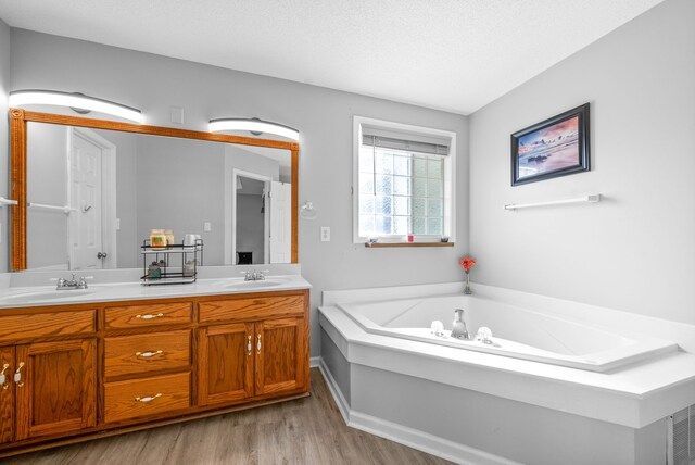 bathroom featuring a textured ceiling, vanity, wood-type flooring, and a tub