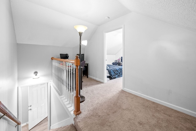 corridor with a textured ceiling, light carpet, and vaulted ceiling