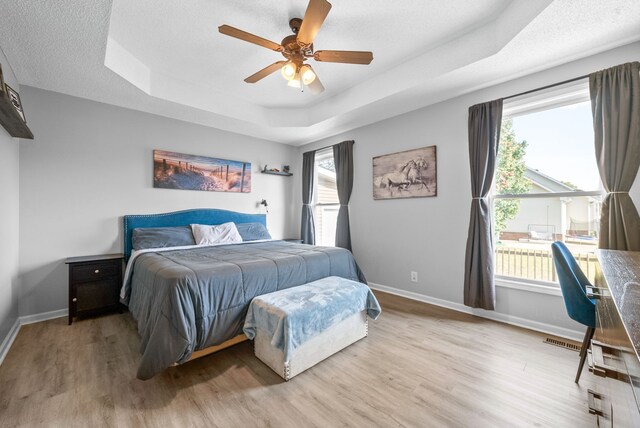 bedroom with ceiling fan, multiple windows, a raised ceiling, and light wood-type flooring