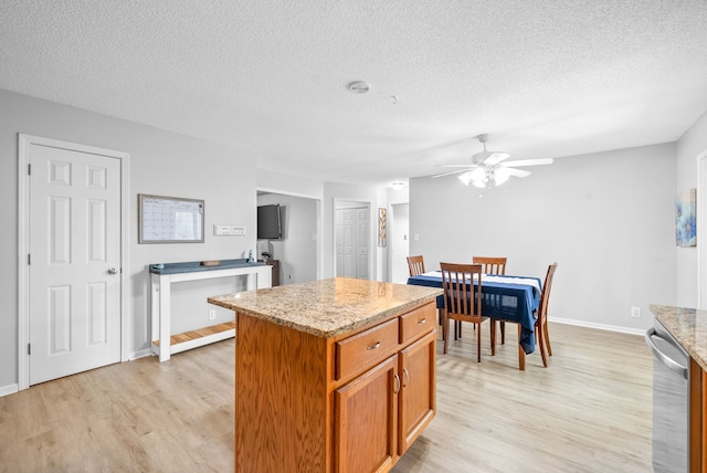 kitchen with light hardwood / wood-style floors, light stone counters, ceiling fan, a textured ceiling, and a kitchen island