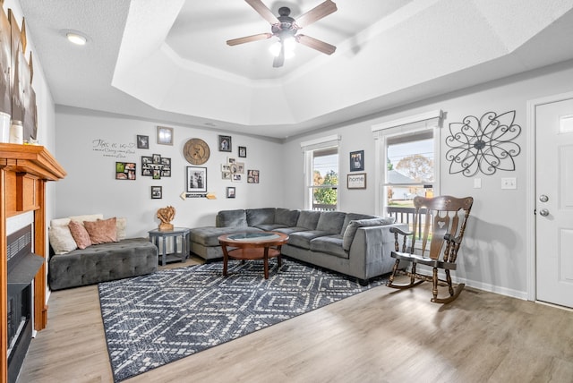 living room with ceiling fan, light wood-type flooring, and a tray ceiling