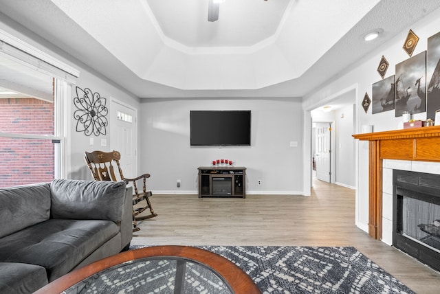 living room with a fireplace, ceiling fan, a raised ceiling, and light hardwood / wood-style flooring