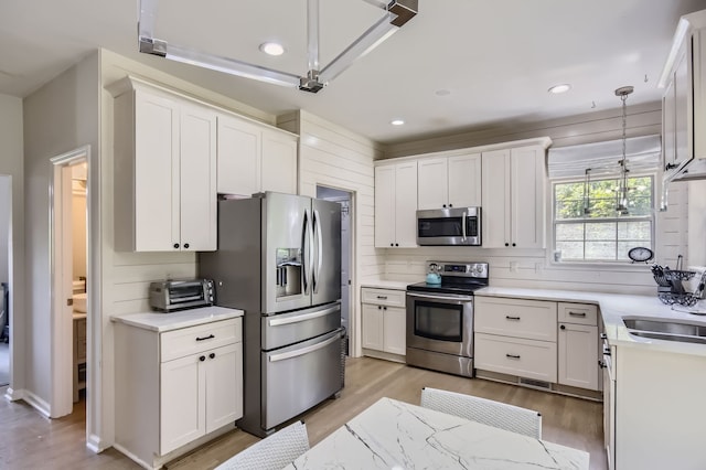 kitchen with hanging light fixtures, white cabinetry, light hardwood / wood-style flooring, and appliances with stainless steel finishes