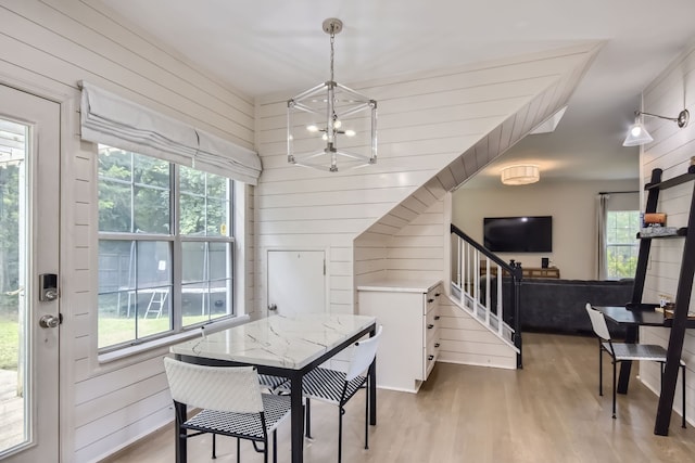 dining area featuring wooden walls, an inviting chandelier, and light hardwood / wood-style floors