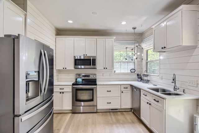 kitchen featuring appliances with stainless steel finishes, decorative light fixtures, sink, light hardwood / wood-style floors, and white cabinets