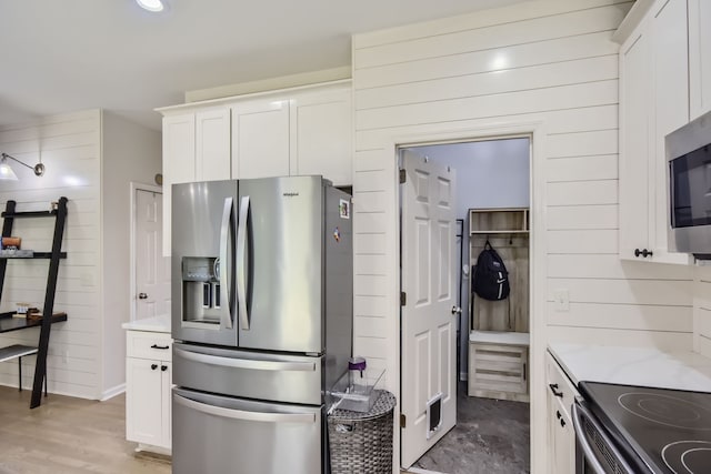 kitchen featuring white cabinets, appliances with stainless steel finishes, wood walls, and light hardwood / wood-style flooring