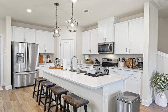 kitchen with stainless steel appliances, white cabinetry, a center island with sink, backsplash, and light hardwood / wood-style flooring