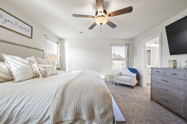 carpeted bedroom with multiple windows, ceiling fan, and ensuite bath