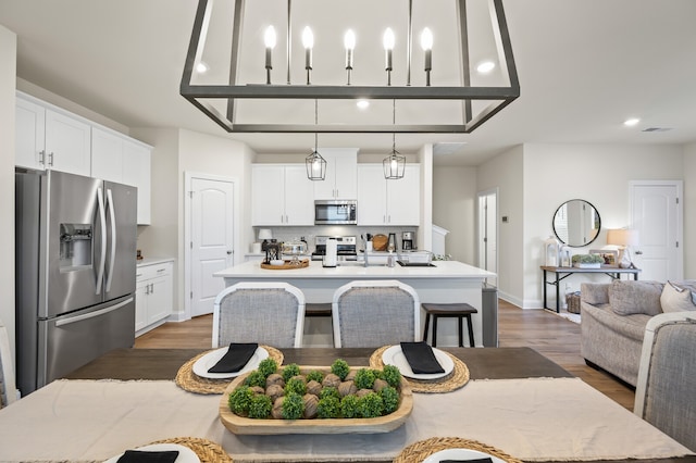 kitchen with white cabinets, a kitchen island with sink, decorative light fixtures, and appliances with stainless steel finishes