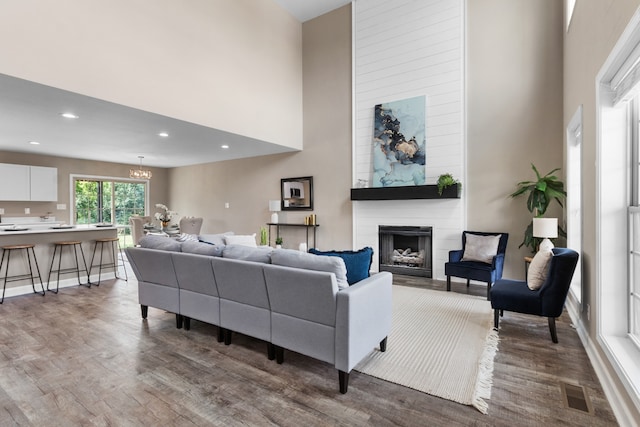 living room featuring dark wood-type flooring, a high ceiling, a fireplace, and an inviting chandelier