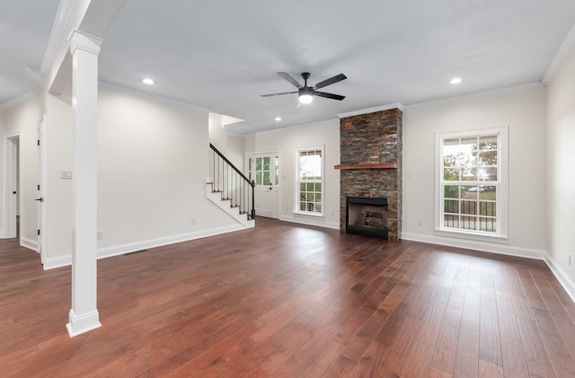 unfurnished living room featuring crown molding, ceiling fan, decorative columns, dark hardwood / wood-style flooring, and a stone fireplace