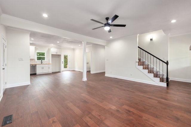 unfurnished living room featuring ornate columns, sink, ceiling fan, crown molding, and dark wood-type flooring