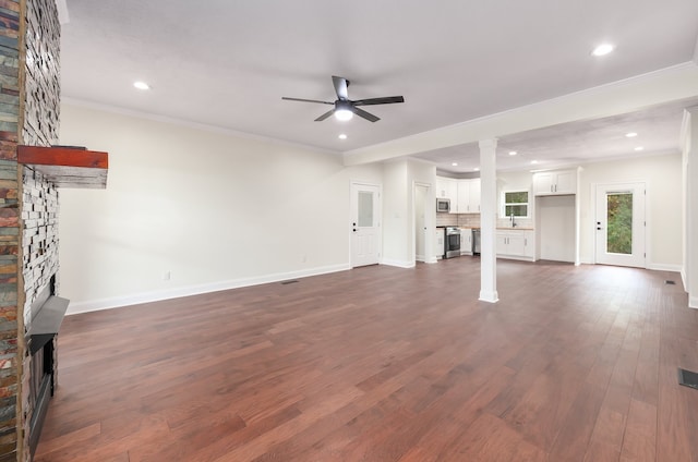 unfurnished living room featuring sink, crown molding, ceiling fan, dark hardwood / wood-style floors, and a stone fireplace