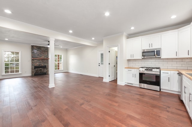 kitchen with appliances with stainless steel finishes, a stone fireplace, white cabinets, backsplash, and ceiling fan