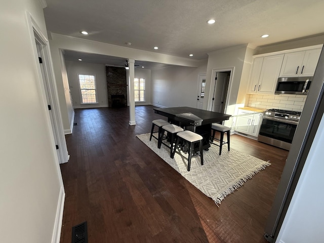 dining room with a stone fireplace, dark wood-type flooring, and ceiling fan