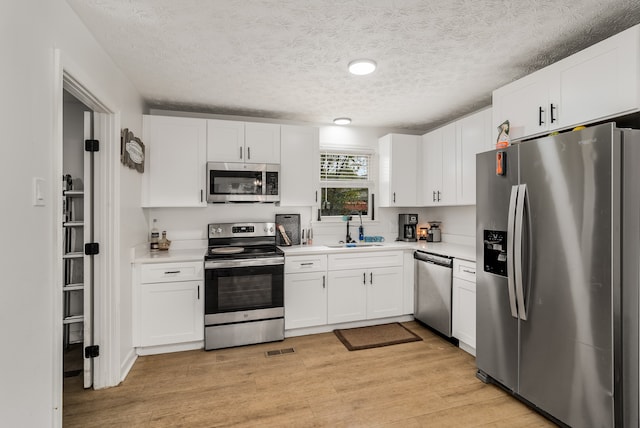 kitchen featuring light hardwood / wood-style floors, sink, appliances with stainless steel finishes, a textured ceiling, and white cabinets