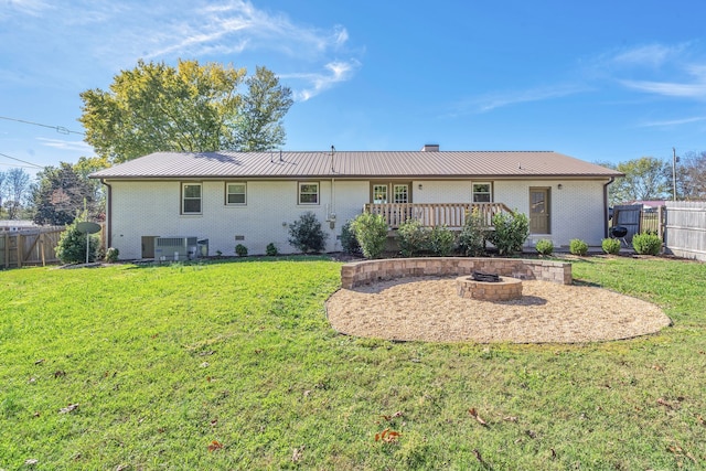 back of property with a lawn, a wooden deck, central air condition unit, and an outdoor fire pit