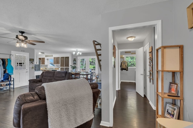 living room with ceiling fan with notable chandelier, dark wood-type flooring, and a textured ceiling