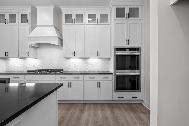 kitchen featuring light wood-type flooring, white cabinets, black gas stovetop, custom exhaust hood, and double oven