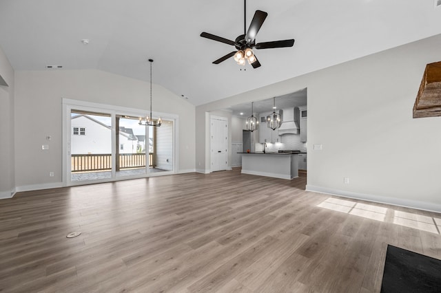 unfurnished living room featuring sink, vaulted ceiling, light hardwood / wood-style floors, and ceiling fan with notable chandelier