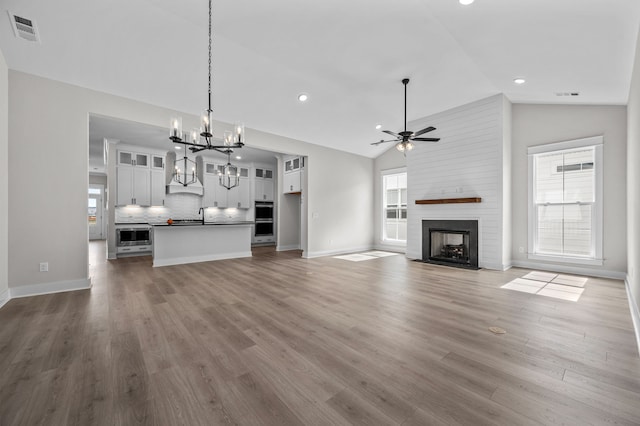 unfurnished living room with dark hardwood / wood-style flooring, high vaulted ceiling, ceiling fan with notable chandelier, and a fireplace