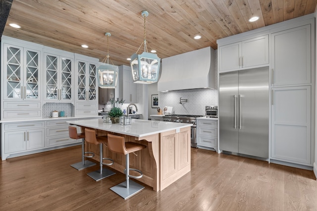 kitchen featuring a kitchen island with sink, premium appliances, white cabinets, custom exhaust hood, and light hardwood / wood-style flooring