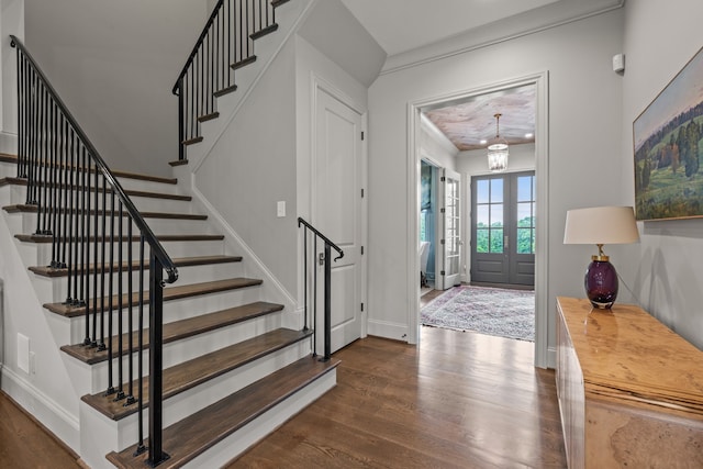 foyer entrance with dark wood-type flooring, a chandelier, crown molding, and french doors