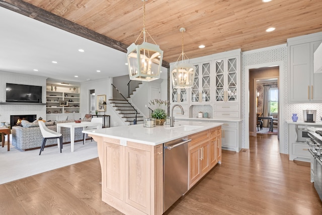 kitchen featuring dishwasher, sink, an island with sink, pendant lighting, and light brown cabinetry